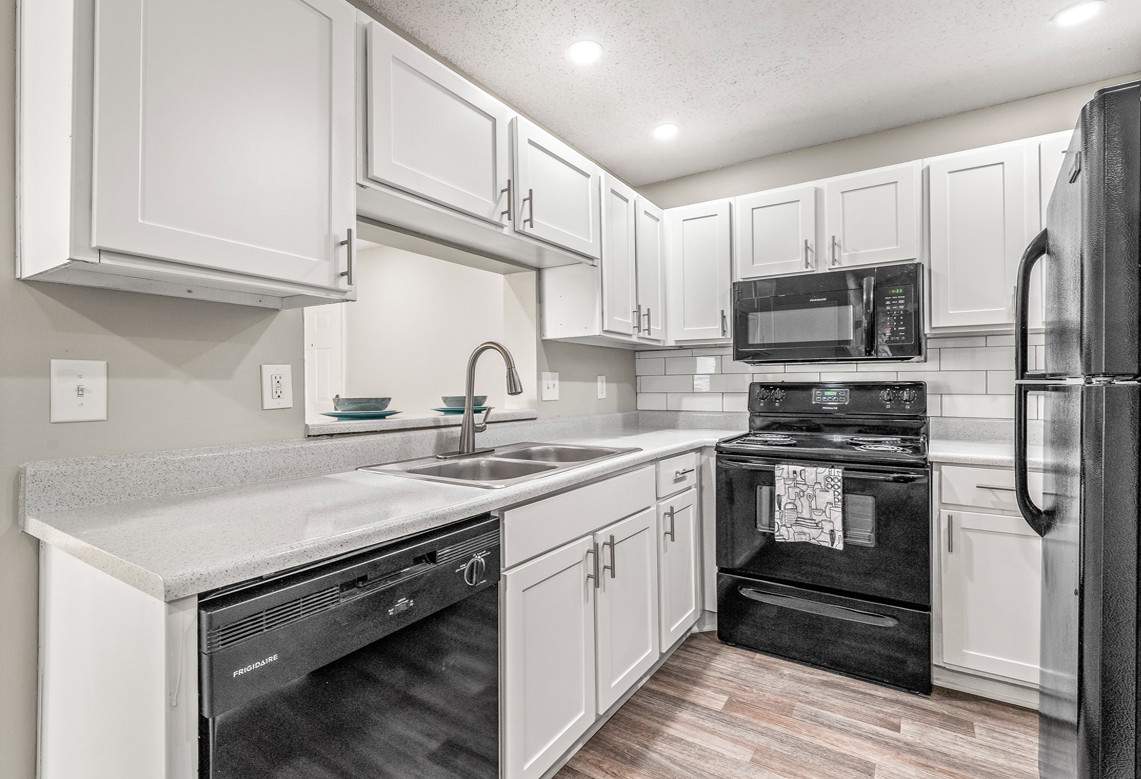 A modern, white-colored kitchen with black appliances, including a black oven, a sink, a microwave, and a refrigerator.