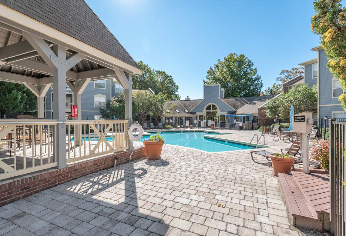 a large swimming pool in a backyard area, with a patio and a gazebo situated near it